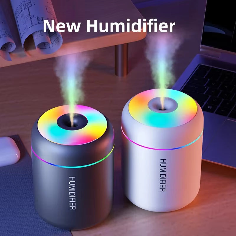 Two colorful humidifiers emitting mist on a desk with a laptop and mouse.