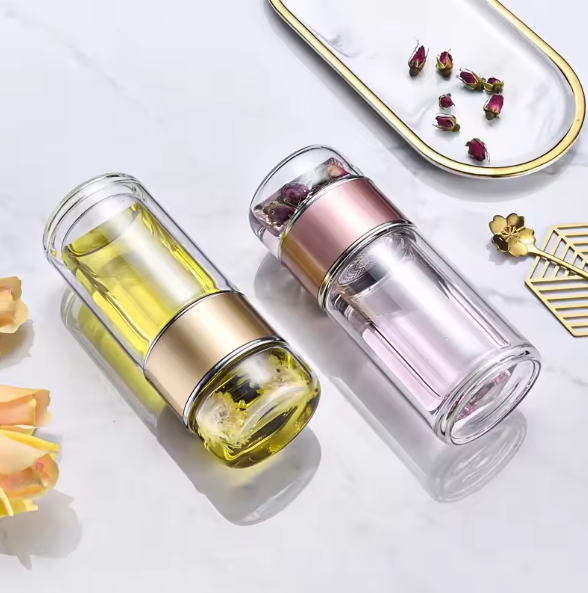 Two Tea Infuser Portable Bottles with gold and pink caps on a white surface with dried flowers.